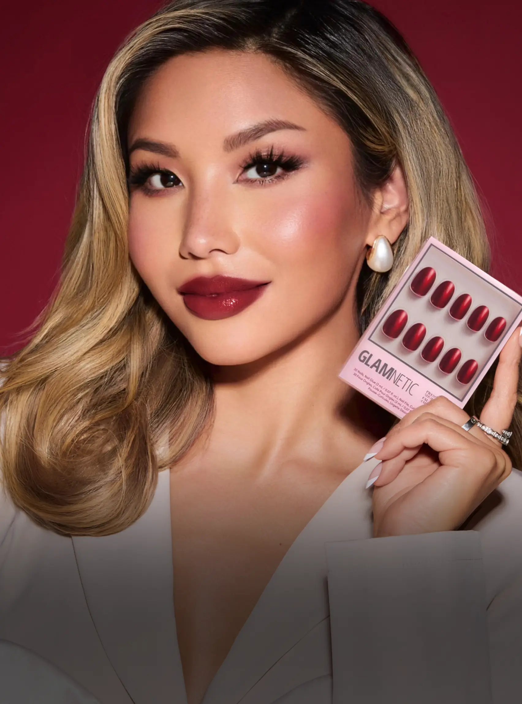 Woman holding a Glamnetic lip product against a red background